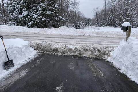 A ridge of compacted gray snow left across the end of a cleared driveway where it meets a county road, tire tracks on the road beyond
